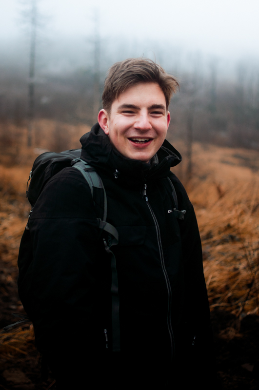 Muž s batohem se usmívá ve vysoké trávě